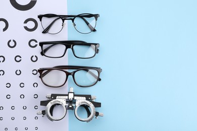 Vision test chart, glasses and trial frame on light blue background, flat lay. Space for text