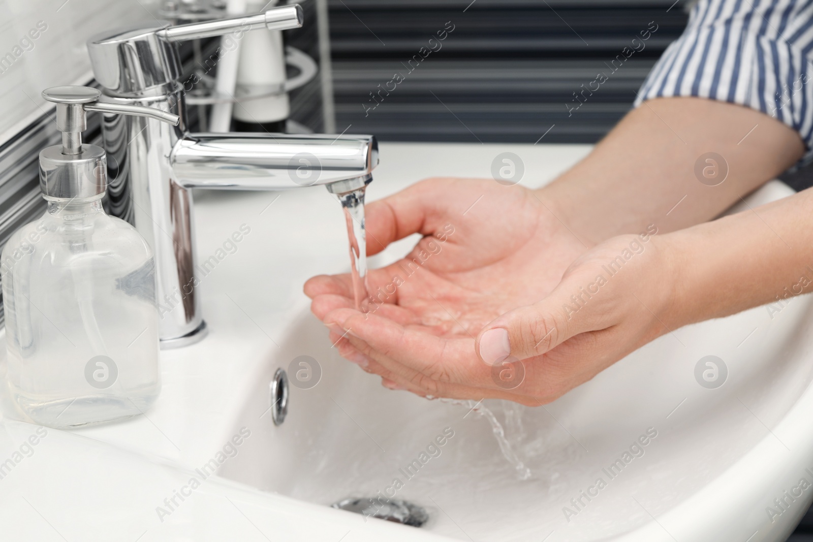 Photo of Man using water tap to wash hands in bathroom, closeup