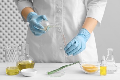 Scientist developing cosmetic oil at white table, closeup