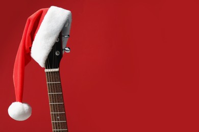 Guitar with Santa hat on red background, space for text