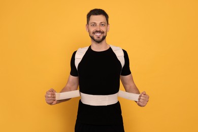 Handsome man with orthopedic corset on orange background