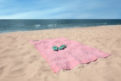 Pink striped beach towel and flip flops on sandy seashore