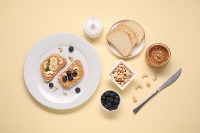 Photo of Toasts with tasty nut butter, blueberries and cashews on beige background, flat lay