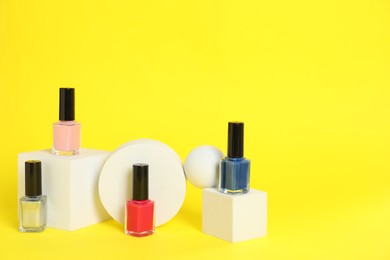 Photo of Stylish presentation of beautiful nail polishes in bottles on yellow background. Space for text