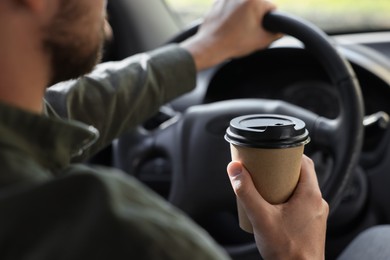 Photo of Coffee to go. Man with paper cup of drink driving his car, closeup