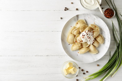 Delicious cooked dumplings with sour cream on white wooden table, flat lay. Space for text