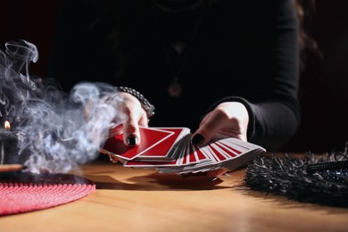 Photo of Soothsayer predicting future with cards at table indoors, closeup