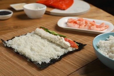 Photo of Unwrapped sushi roll with rice, cucumber, cheese and salmon on wooden table, closeup