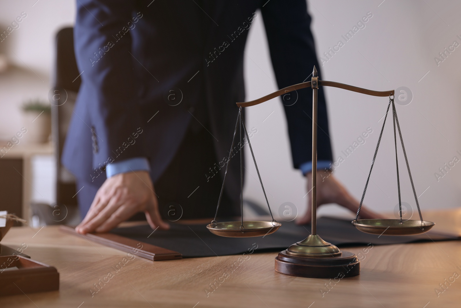 Photo of Male lawyer at table in office, focus on scales of justice