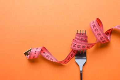 Photo of Fork with measuring tape on orange background, top view with space for text. Diet concept