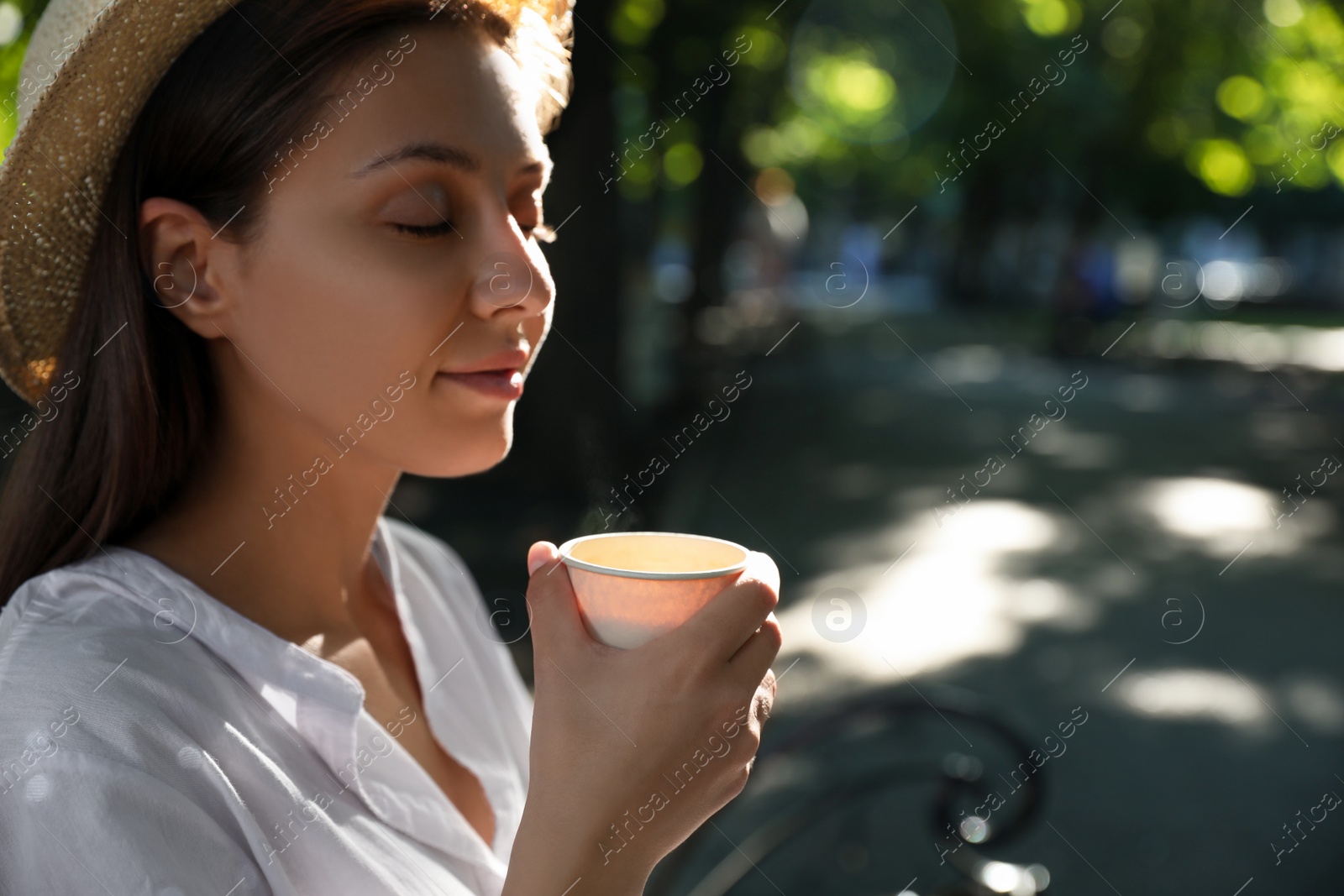 Photo of Beautiful young woman with drink in park on sunny day, space for text