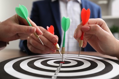Photo of Business targeting concept. People with darts aiming at dartboard at table indoors, closeup