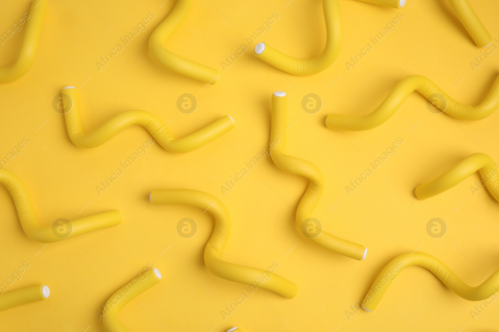 Photo of Curling rods on yellow background, flat lay. Hair styling tool