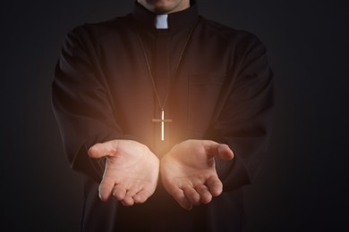 Priest reaching out his hands with holy light on black background, closeup