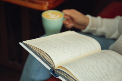 Photo of Woman with cup of coffee reading book indoors, closeup