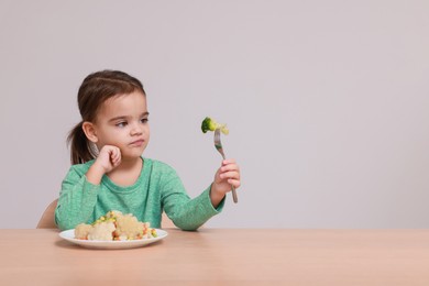 Photo of Cute little girl refusing to eat vegetable salad at table on grey background, space for text