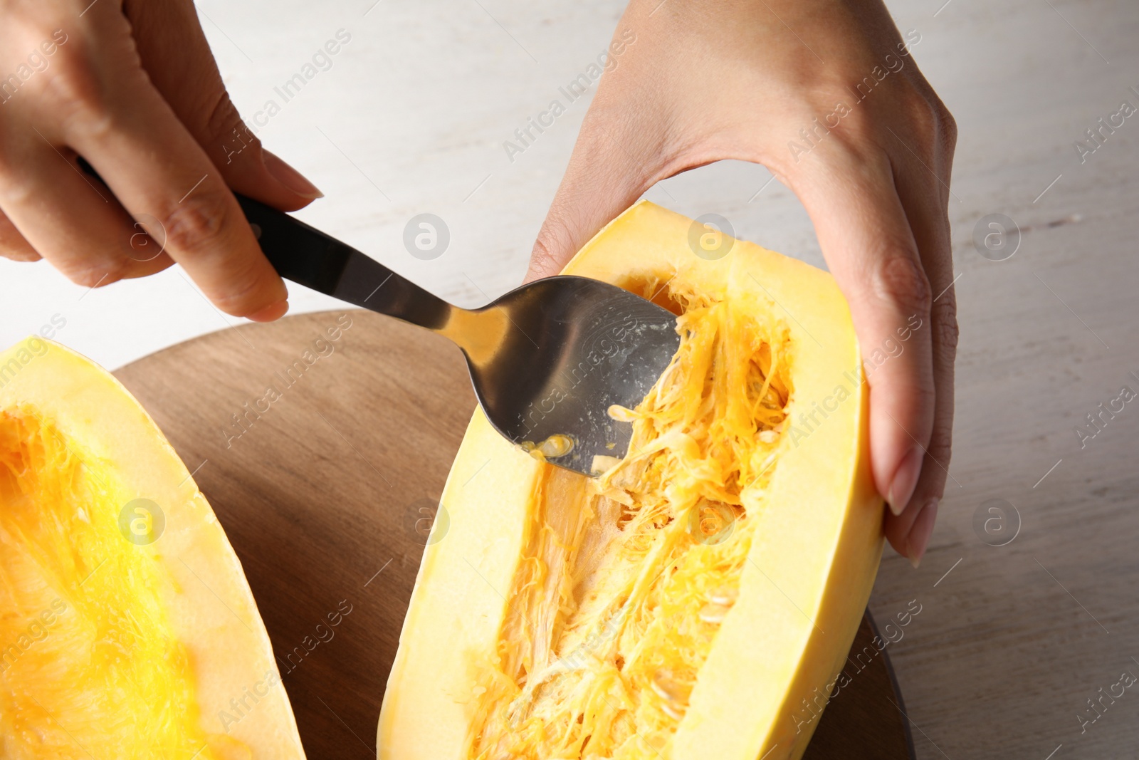 Photo of Woman removing seeds from spaghetti squash on table, closeup