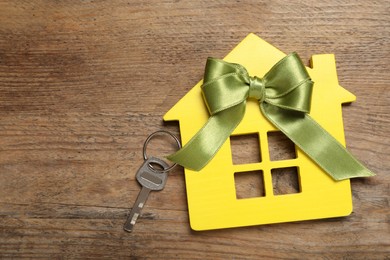 Yellow house model with key on wooden table, top view and space for text. Housewarming party