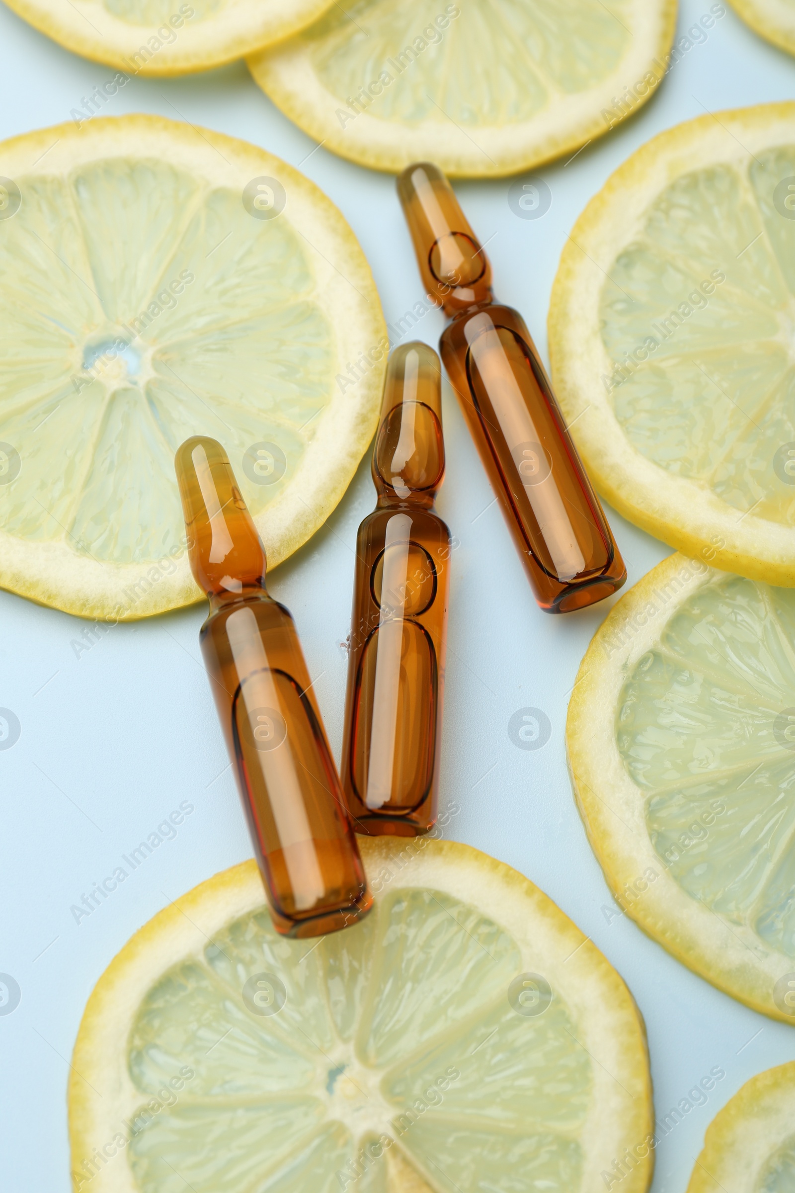 Photo of Skincare ampoules with vitamin C and slices of lemon on light blue background, flat lay