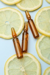 Skincare ampoules with vitamin C and slices of lemon on light blue background, flat lay