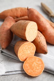 Photo of Whole and cut ripe sweet potatoes on grey table