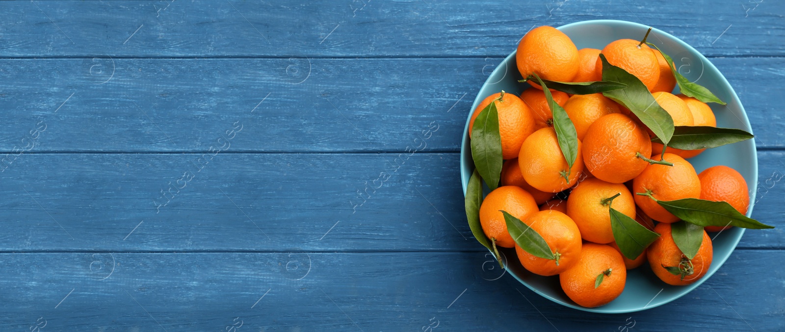 Image of Fresh ripe tangerines and green leaves on blue wooden table, top view with space for text. Banner design