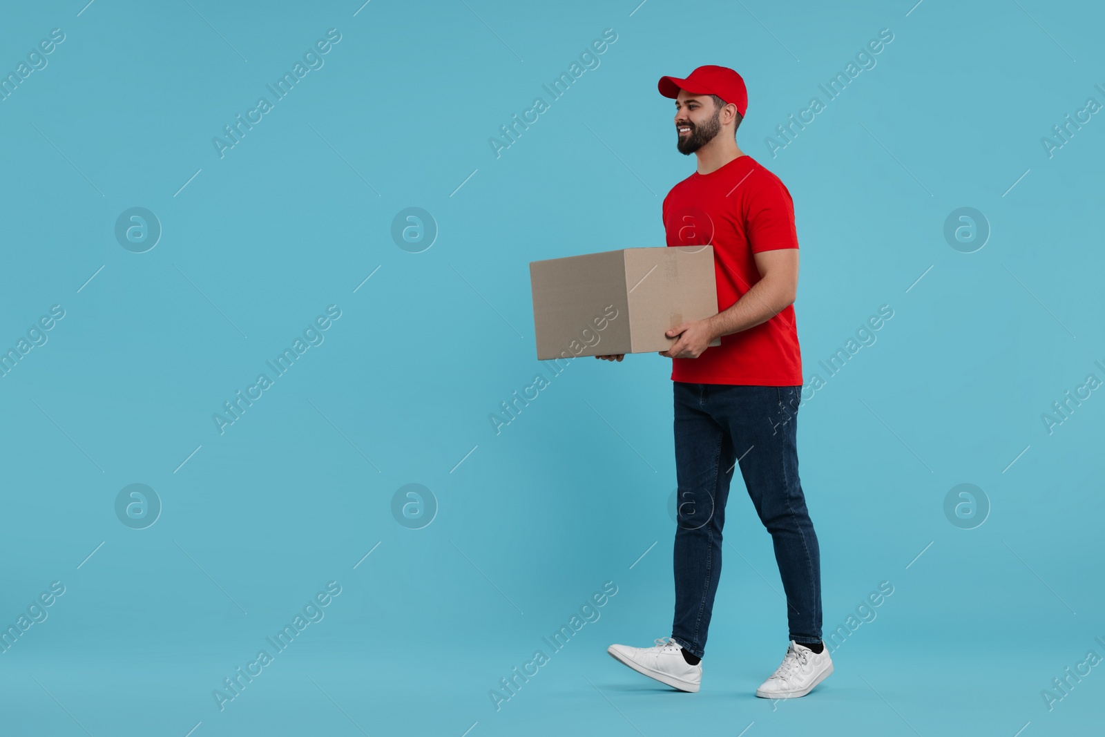 Photo of Happy young courier with parcel on light blue background, space for text