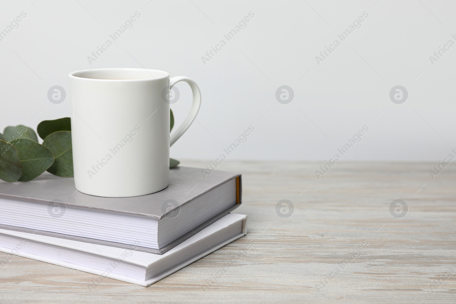 White ceramic mug, stack of books and eucalyptus branch on white wooden table, space for text Photo of White ceramic mug, stack of books and eucalyptus branch on white wooden table, space for text