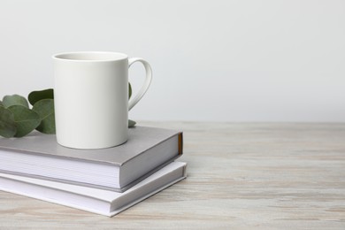 Photo of White ceramic mug, stack of books and eucalyptus branch on white wooden table, space for text