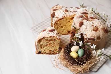 Photo of Delicious Italian Easter dove cake (traditional Colomba di Pasqua), decorative nest with painted eggs and flowering branches on white table. Space for text