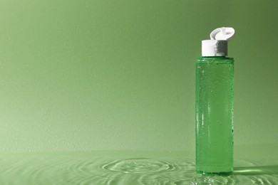 Photo of Wet bottle of micellar water on green background, space for text