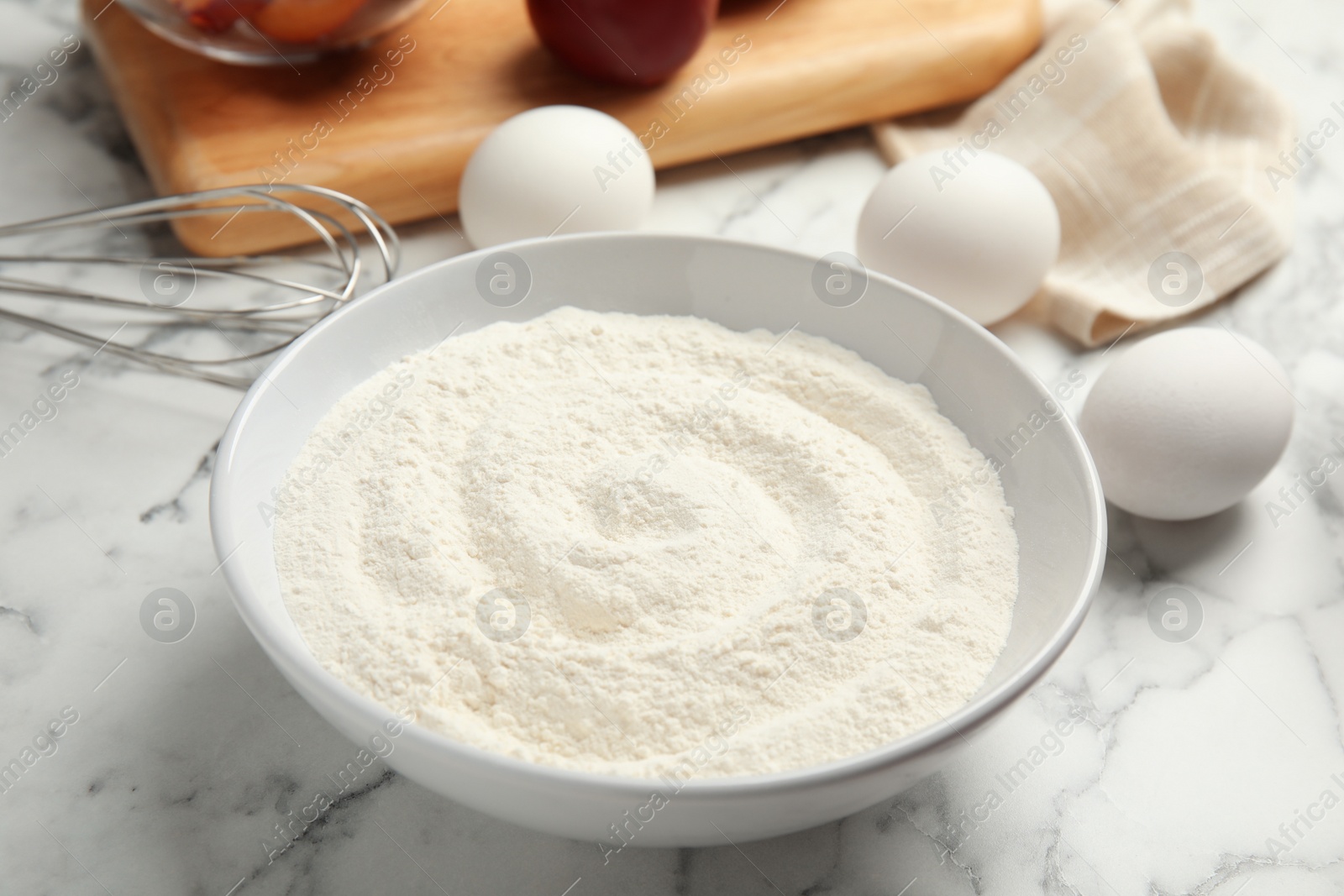 Photo of Bowl with flour on white marble table, closeup. Cooking of delicious plum cake