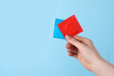 Photo of Woman holding condoms on light blue background, closeup. Space for text