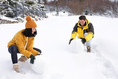 Happy couple making snowman outdoors. Winter vacation