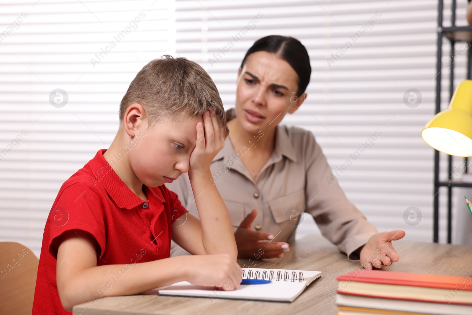 Photo of Dyslexia problem. Annoyed mother helping son with homework at table indoors, selective focus