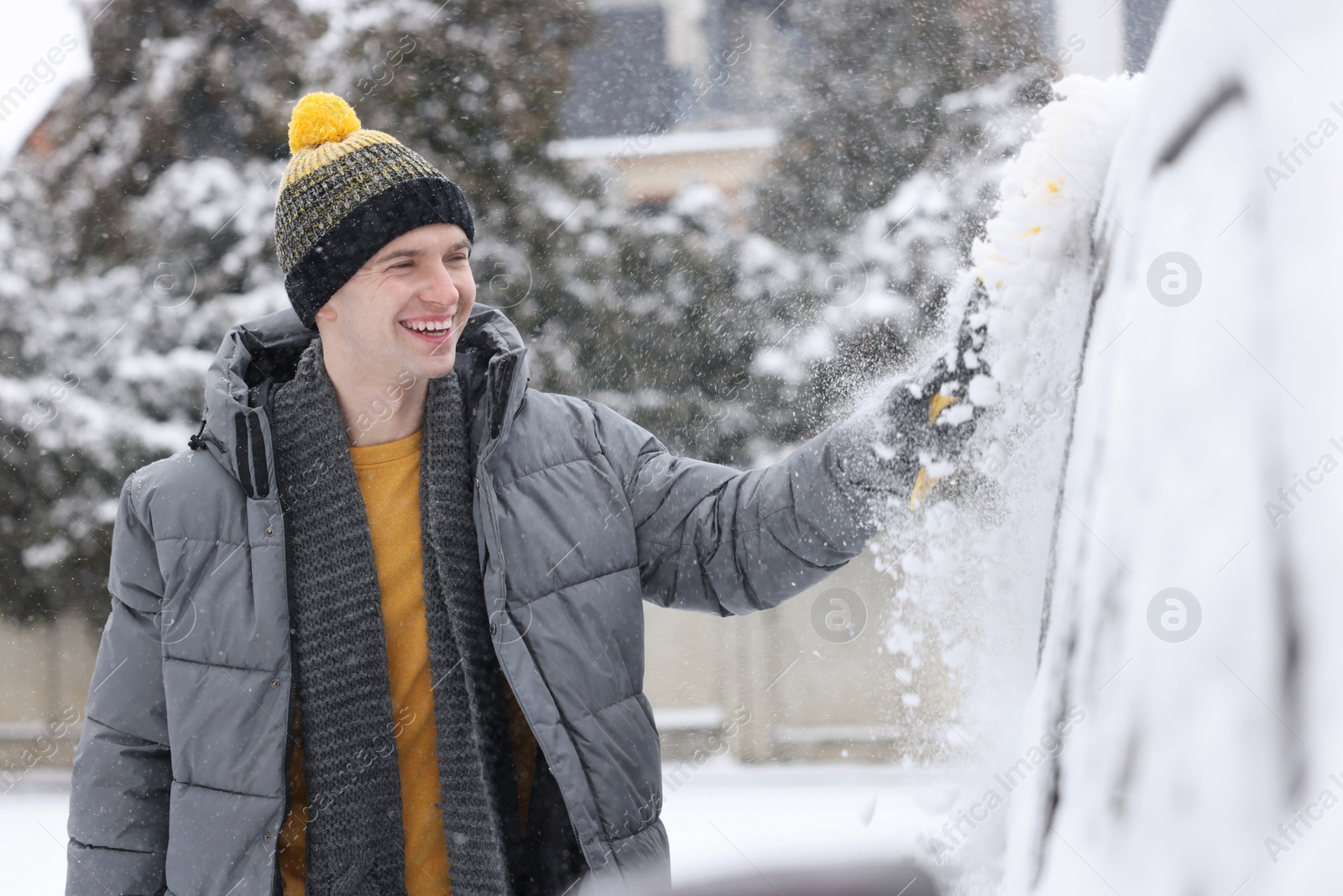 Photo of Man cleaning snow from car with brush outdoors