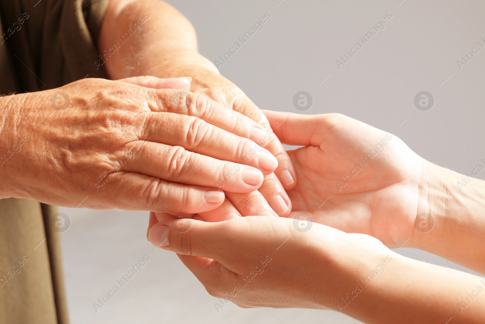 Photo of Helping hands on grey background, closeup. Elderly care concept