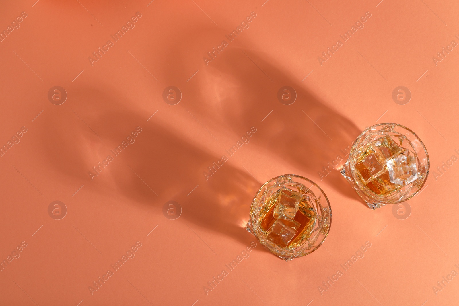 Photo of Whiskey with ice cubes in glasses on coral table, flat lay. Space for text