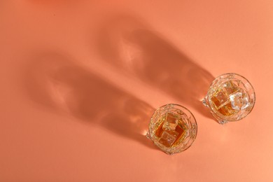 Photo of Whiskey with ice cubes in glasses on coral table, flat lay. Space for text