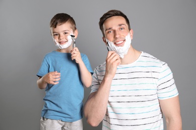 Photo of Dad shaving and little son imitating him on color background