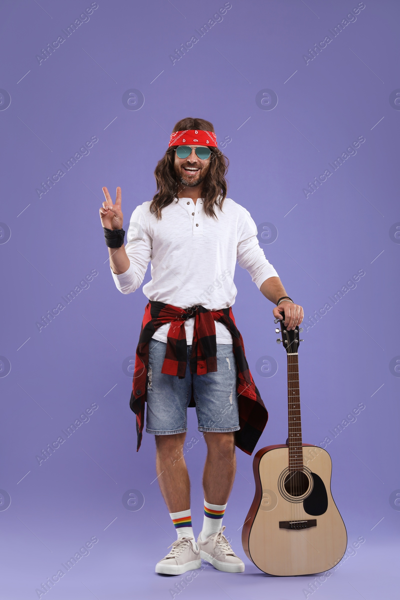 Photo of Stylish hippie man with guitar showing V-sign on violet background