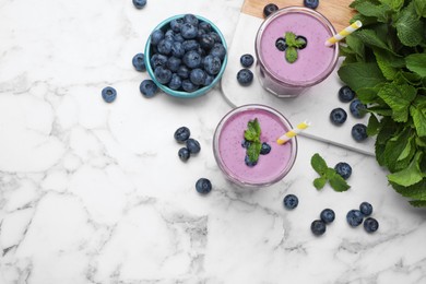 Glasses of blueberry smoothie with mint and fresh berries on white marble table, flat lay. Space for text