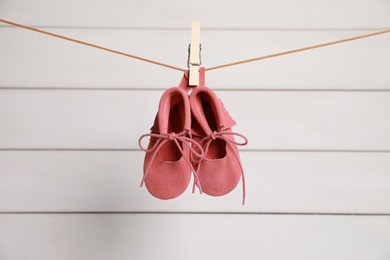 Pink baby shoes drying on washing line against white wall