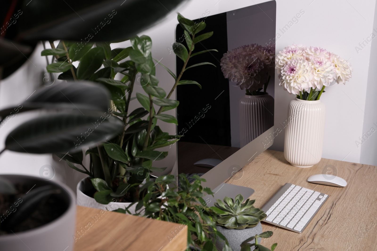 Photo of Comfortable workplace with modern computer, green houseplants and beautiful flowers on wooden table indoors