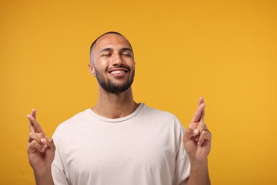 Photo of Happy man crossing his fingers on orange background. Space for text