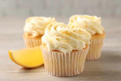 Photo of Tasty cupcakes with cream, zest and lemon slice on light wooden table, closeup