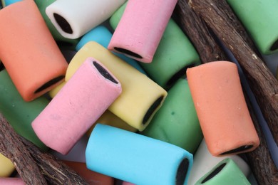 Many tasty candies and dried sticks of liquorice root on white background, flat lay