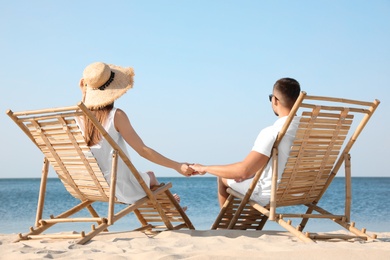 Photo of Young couple relaxing in deck chairs on beach