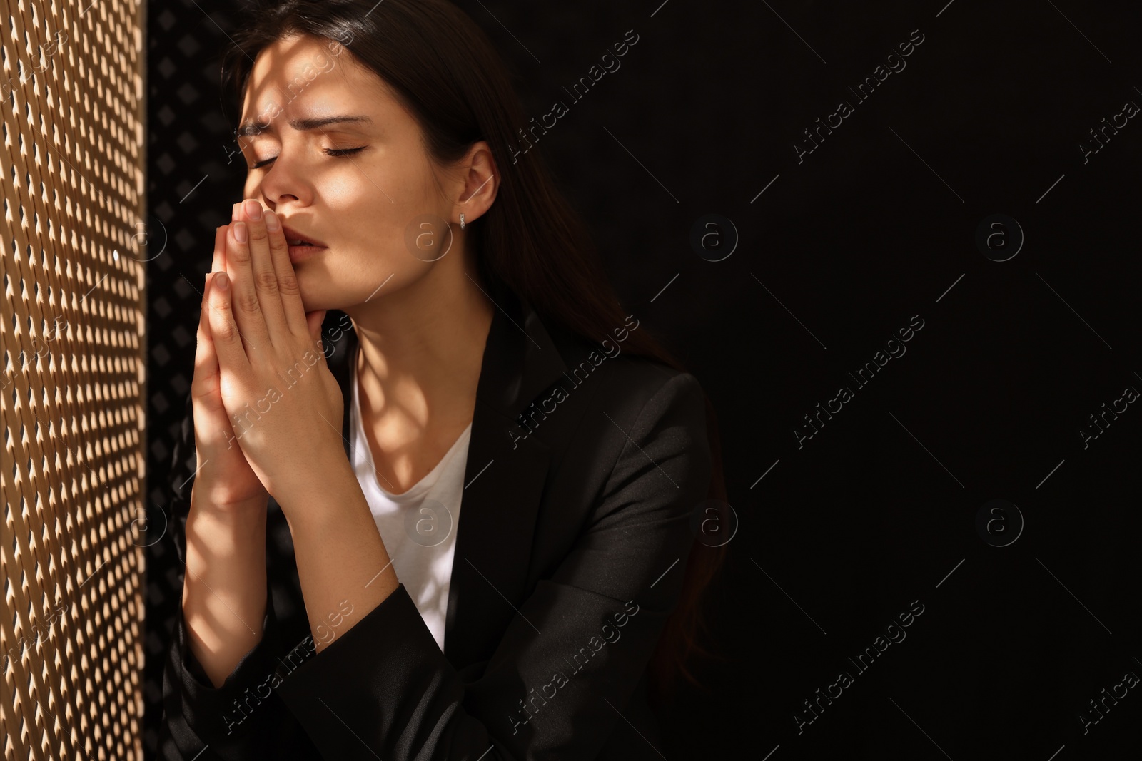 Photo of Woman praying to God during confession in booth, space for text