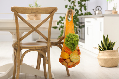 Photo of Net bag with vegetables hanging on wooden chair in kitchen